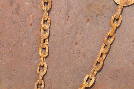 Close-up of the links in a corroded gold colored chain on a rusty red metal background.
