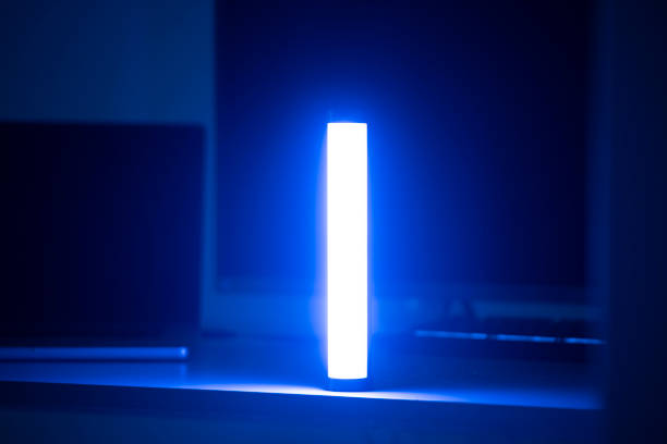 A single blue light stick emits a neon glow, creating a tranquil atmosphere in a dimly lit room with vertical blinds.