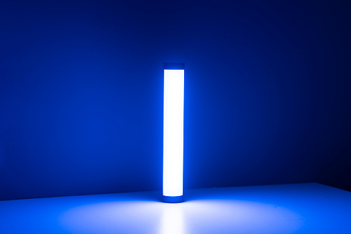 A single blue light stick emits a neon glow, creating a tranquil atmosphere in a dimly lit room with vertical blinds.