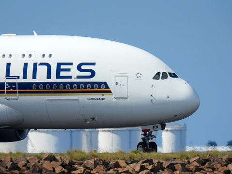 A Singapore Airlines Airbus A380-841 plane, registration 9V-SKN, taxiing after landing at Sydney Kingsford-Smith Airport as flight SQ231 from Singapore.   In the background are fuel storage tanks.  This image was taken from near Kyeemagh Beach, Botany Bay on a hot and sunny morning on 24 March 2024.