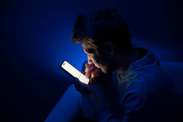 istock A young person appears to be having an eye problem as she squints while looking at her phone screen in a poorly lit room, suggesting the stress of poor eyesight when viewing devices at a close distance. 2110890303