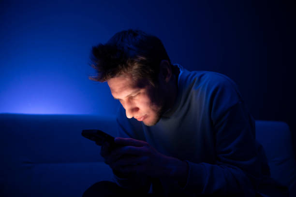istock A young person appears to be having an eye problem as she squints while looking at her phone screen in a poorly lit room, suggesting the stress of poor eyesight when viewing devices at a close distance. 2110890304