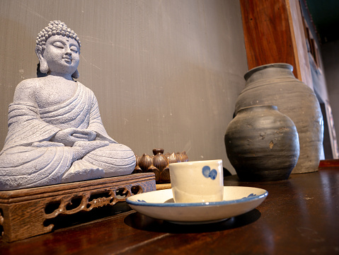 White Stone Buddha Sitting with Hands Clasped on a Wooden Base The Front has a Incense Stick in The Old Wooden Table