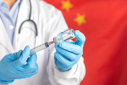 A doctor holds a syringe with a vaccine bottle standing on the Chinese flag background. Medical concept.