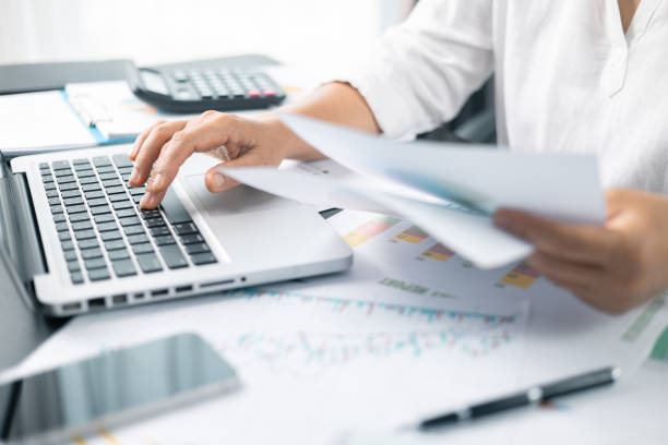 istock Woman analyze document in her hands. Businesswoman analyst working at office on laptop while sitting at wooden table. Business financing accounting banking concept. finance accounting. 2111000304