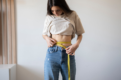 Woman in Casual Attire Measuring Her Waistline using yellow tape Indoors