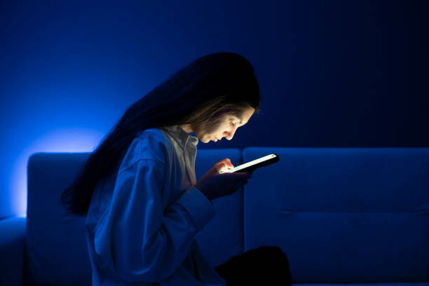 istock A young person appears to be having an eye problem as she squints while looking at her phone screen in a poorly lit room, suggesting the stress of poor eyesight when viewing devices at a close distance. 2111017277