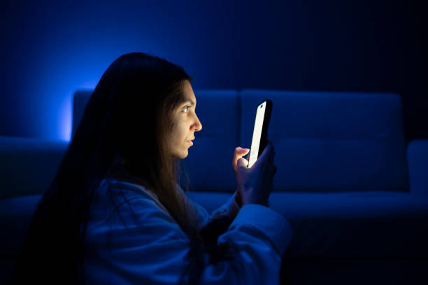 A young person appears to be having an eye problem as she squints while looking at her phone screen in a poorly lit room, suggesting the stress of poor eyesight when viewing devices at a close distance. una persona joven parece tener un problema ocular mientras entrecierra los ojos mientras mira la pantalla de su teléfono en una habitación mal iluminada, lo que sugiere el estrés de la mala vista cuando ve dispositivos a corta distancia.