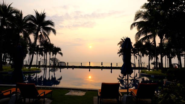 Beachfront resort with poolside, lounge chairs and white parasol on sunny day
