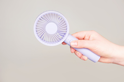 Female hand holding a small fan on gray background close up.