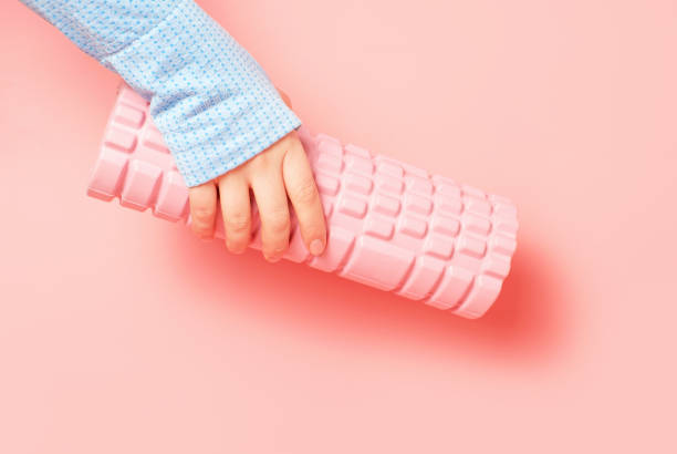 istock Female hand holding a massage roll on pink background close-up. 2111056590