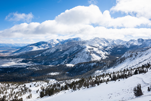 A view of snowy mountains and puffy clouds on a sunny winter day in Mammoth Lakes, CA