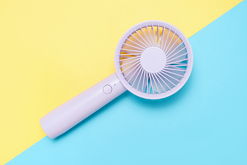 Small portable mini fans on blue and yellow background close up.
