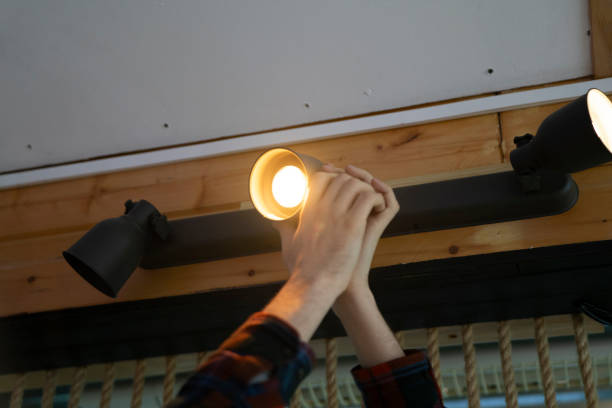 istock Man Changing a Burnt-Out Light Bulb on a spot light construction in an Office Ceiling Fixture 2111070981