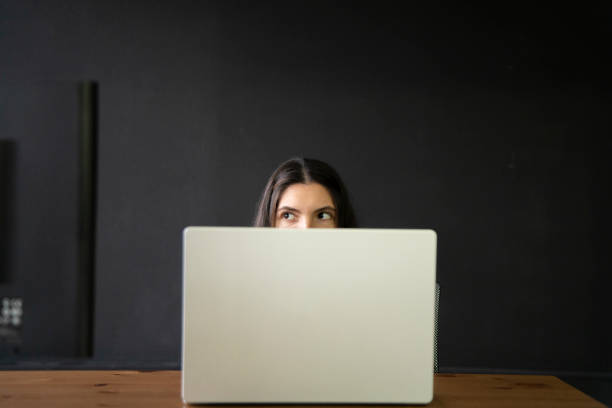 istock Office Worker Sneaking a Peek Above Laptop in a Modern Workspace During Daytime, hiding from boss 2111071021