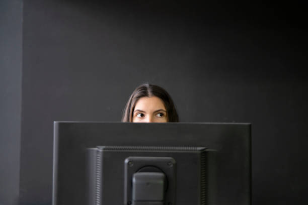 Office Worker Sneaking a Peek Above Laptop in a Modern Workspace During Daytime, hiding from boss