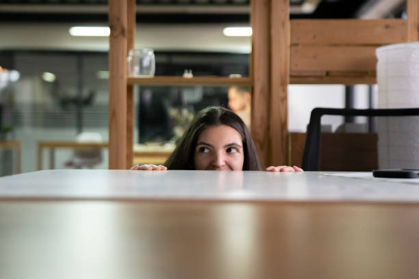 istock Office Worker Sneaking a Peek Above Laptop in a Modern Workspace During Daytime, hiding from boss 2111071037