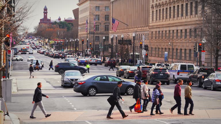 Crowd pedestrian and tourist walking and crossing road intersection with traffic in rush hour among modern buildings of Downtown Washington, D.C., United States