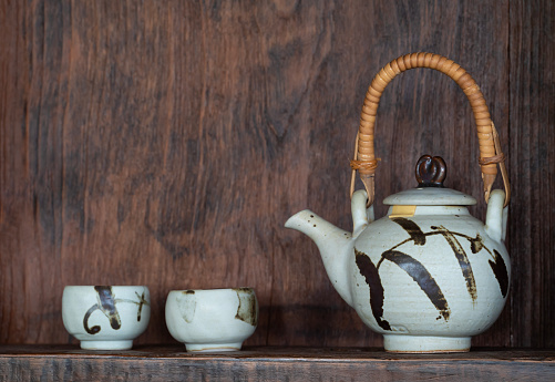 Close-up of handmade teapot and cups with natural light on a wooden background. Copy space for text.