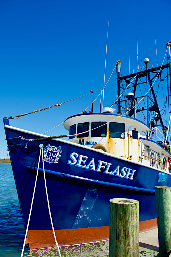 Chincoteague, Virginia, USA - March 21, 2024: The “Seaflash” shrimp trawler docked at the Robert N. Reed Downtown Waterfront Park in the Town of Chincoteague on a sunny afternoon.