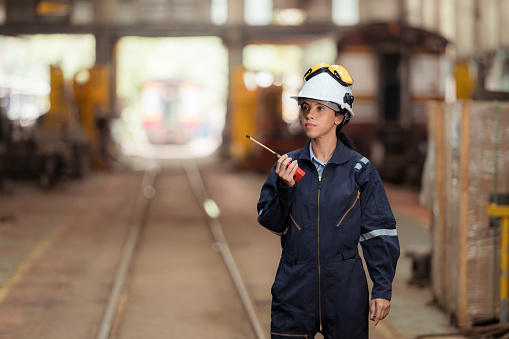 Portrait of railway technician worker in safety vest and helmet working and using a walkie talkie at train repair station