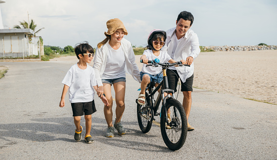 Under golden glow of a sunset a happy father mother and daughter create lasting memories on a summer road trip. Teaching learning and enjoying bicycle riding on a sandy beach perfect family portrait.
