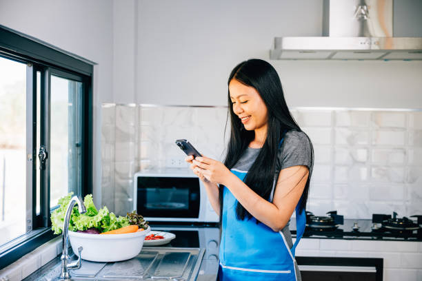 istock Smiling woman reads messages on her cellphone leaning on the kitchen 2111201010