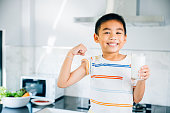 Portrait of smiling Asian little boy holding milk in kitchen. Cute son enjoys drink, radiating joy. Preschool child savoring calcium-rich liquid, feeling happy at home give me.