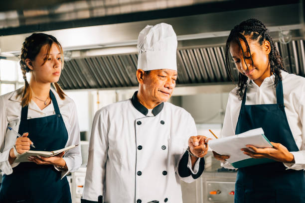 istock In a restaurant kitchen senior Asian chef educates multiracial students. Emphasizing teamwork learning and note-taking. Professional training session. Food Edocation 2111201540
