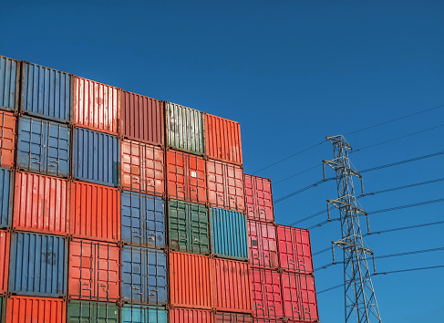 Stack of shipping containers with electricity pylon in distance against a deep blue sky