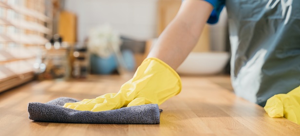 Maid in protective glove cleans wood table in cozy kitchen. Using professional cleaning products for perfect home tidiness. Cleaner working safety glove hygiene routine. Maid housekeeping concept.