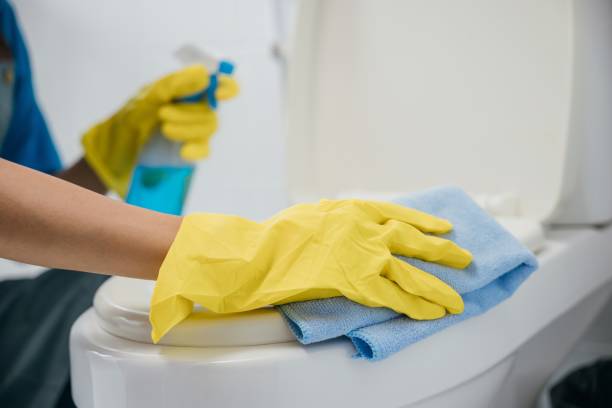 Dedicated maid in rubber gloves scrubs toilet seat with cloth ensuring hygiene in the bathroom. Her focus on cleanliness highlights the essence of housekeeping. Housekeeper healthcare concept A maid wears yellow gloves meticulously cleaning toilet seat with cloth. Her commitment to hygiene and purity emphasizes housekeeping in the bathroom. Housekeeper healthcare concept deep cleaning services stock pictures, royalty-free photos & images