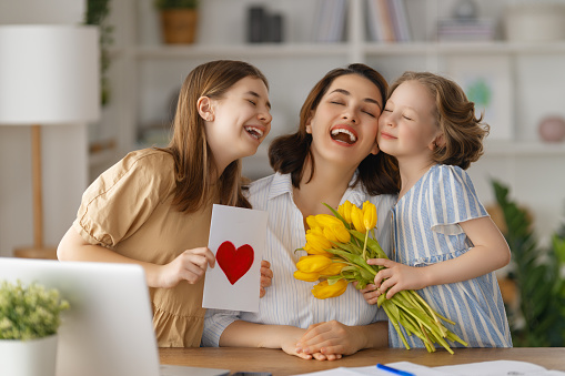 Daughter hugs mother, focus on tulip bouquet.