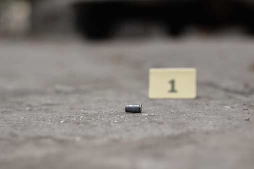 Pistol bullet shell on cement floor with blurred number one yellow paper, concept for investigation and crime by using gun, soft focus.