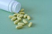 Yellow pills spilling out of pill bottle on green background. Focus on foreground.