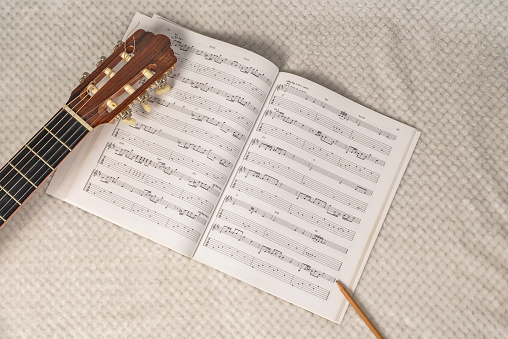 Image depicting the writing and composition of a guitar sheet music with a sheet music, a guitar neck and a wooden pencil.