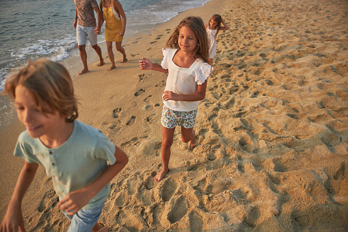 A family run hand in hand down a tropical paradise beach during sunset.