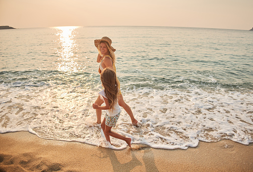 Mother and daughter run hand in hand down a tropical paradise beach during sunset.