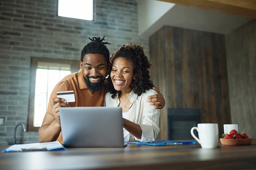 Happy African American couple enjoying while shopping online over a computer at home.