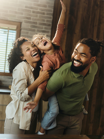Happy African American parents having fun with their small girl at home. Father is piggybacking daughter.