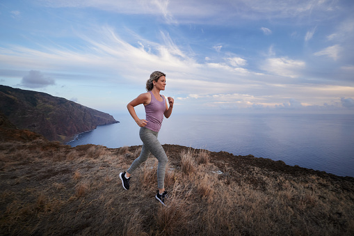 Determined athletic woman jogging during sports training on a cliff above the sea. Copy space.