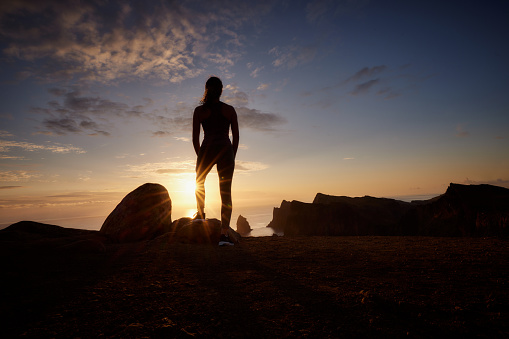 Back view of a woman standing on a cliff of Ponta De Sao Lourenco at sunset. Copy space.