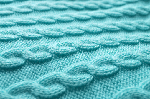 Macro close-up: delicate turquoise knitted fabric with visible stitches resembling a braided pattern. Side view: angled perspective