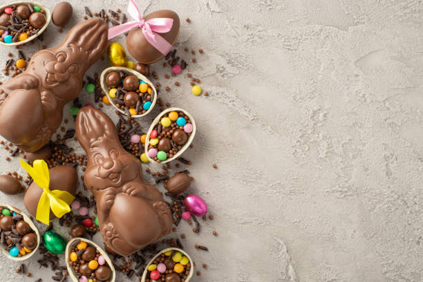 istock Chic Easter confectionery set-up. View from top captures chocolate eggs adorned with bows, filled with assorted candies, chocolate rabbits, confetti staged on concrete surface with space for copy 2111423779
