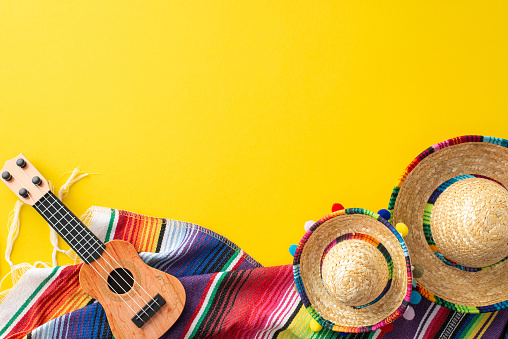Cinco de Mayo assortment. Top view picture of party gear: tiny hats, a crafted vihuela, a colorful serape, placed on a vibrant yellow setting