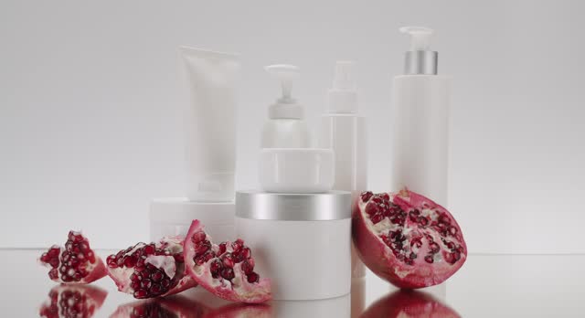 White tubes with pomegranate fruits for cosmetics on a white background