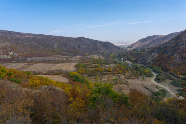 View of the mountains, river, fields and valley from the hill. Autumn colors of red, yellow, green and orange leaves and bushes. Clear blue sky and clouds. Hills and peaks.
