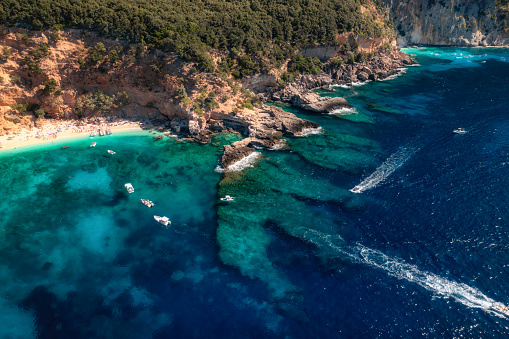 Aerial view of seascape with stone coastline and small beach with crowd of people. Sea coast with blue, turquoise clear water. Islands of Sardinia in Italy. Summer holiday background