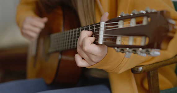 Close-up of girl hand's playing guitar of music lesson at home.
