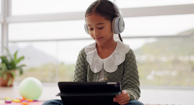 Girl child, headphones and tablet in home, floor and listen to music for motivation, creativity or education. Kid, audio tech and streaming for elearning video, study or online course in family house